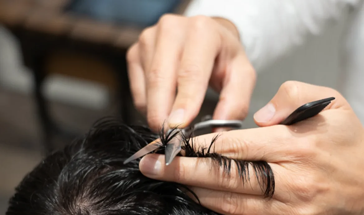 Barbiere al lavoro sui capelli scuri di un cliente, controllo della cute per la caduta dei capelli in autunno