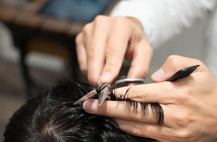 Barbiere al lavoro sui capelli scuri di un cliente, controllo della cute per la caduta dei capelli in autunno