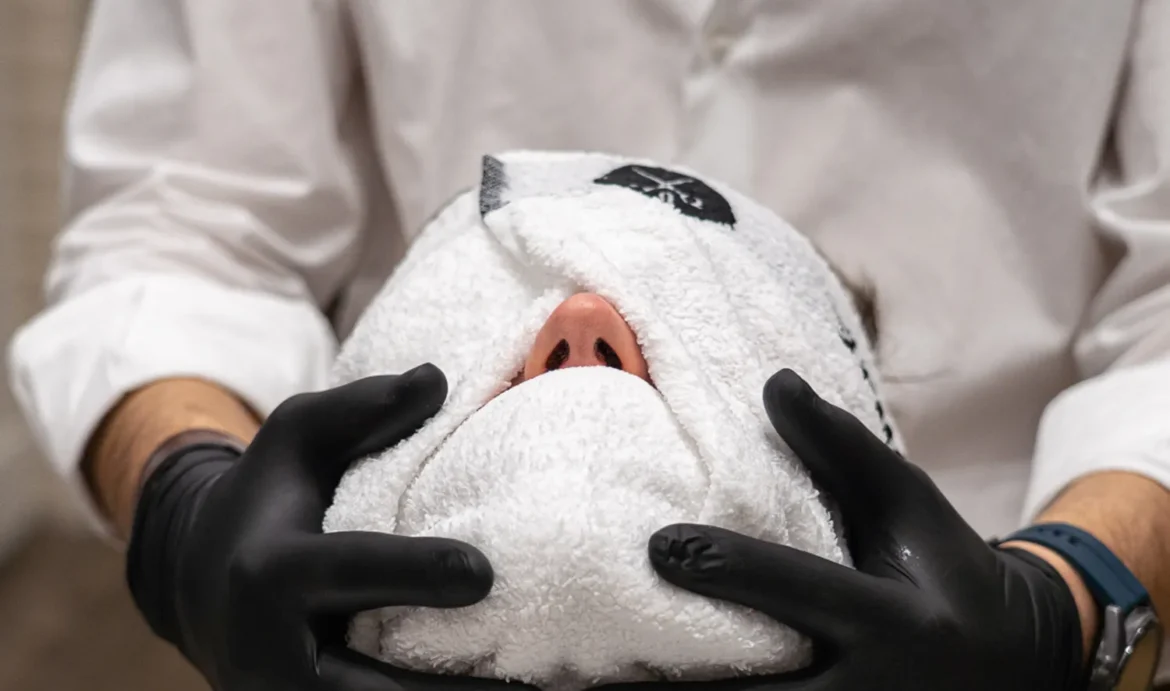 Panno caldo sul viso di un cliente, un momento di relax dal barbiere