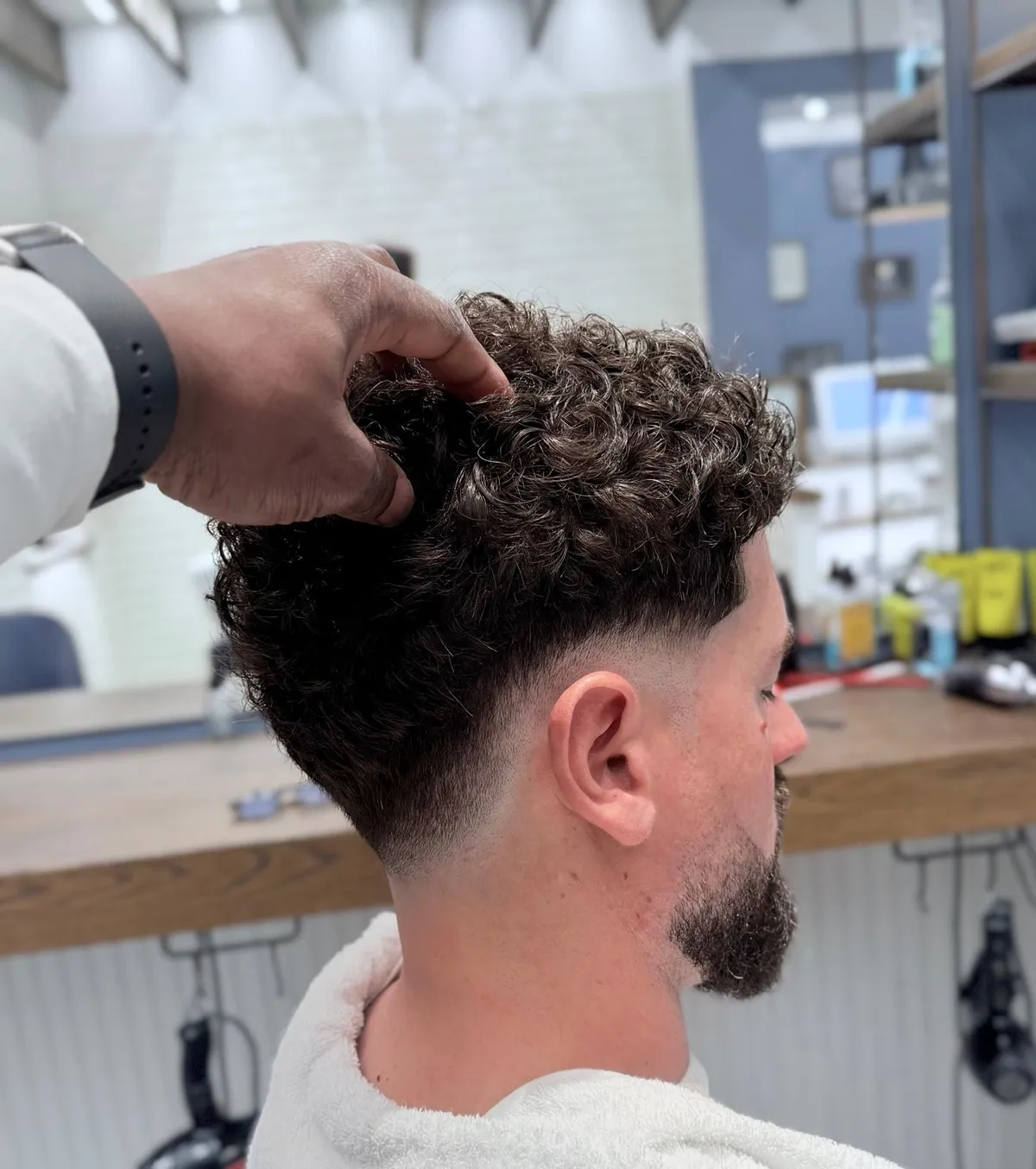 Mani di un barbiere che modellano i capelli ricci di un cliente, styling con cera a tenuta forte